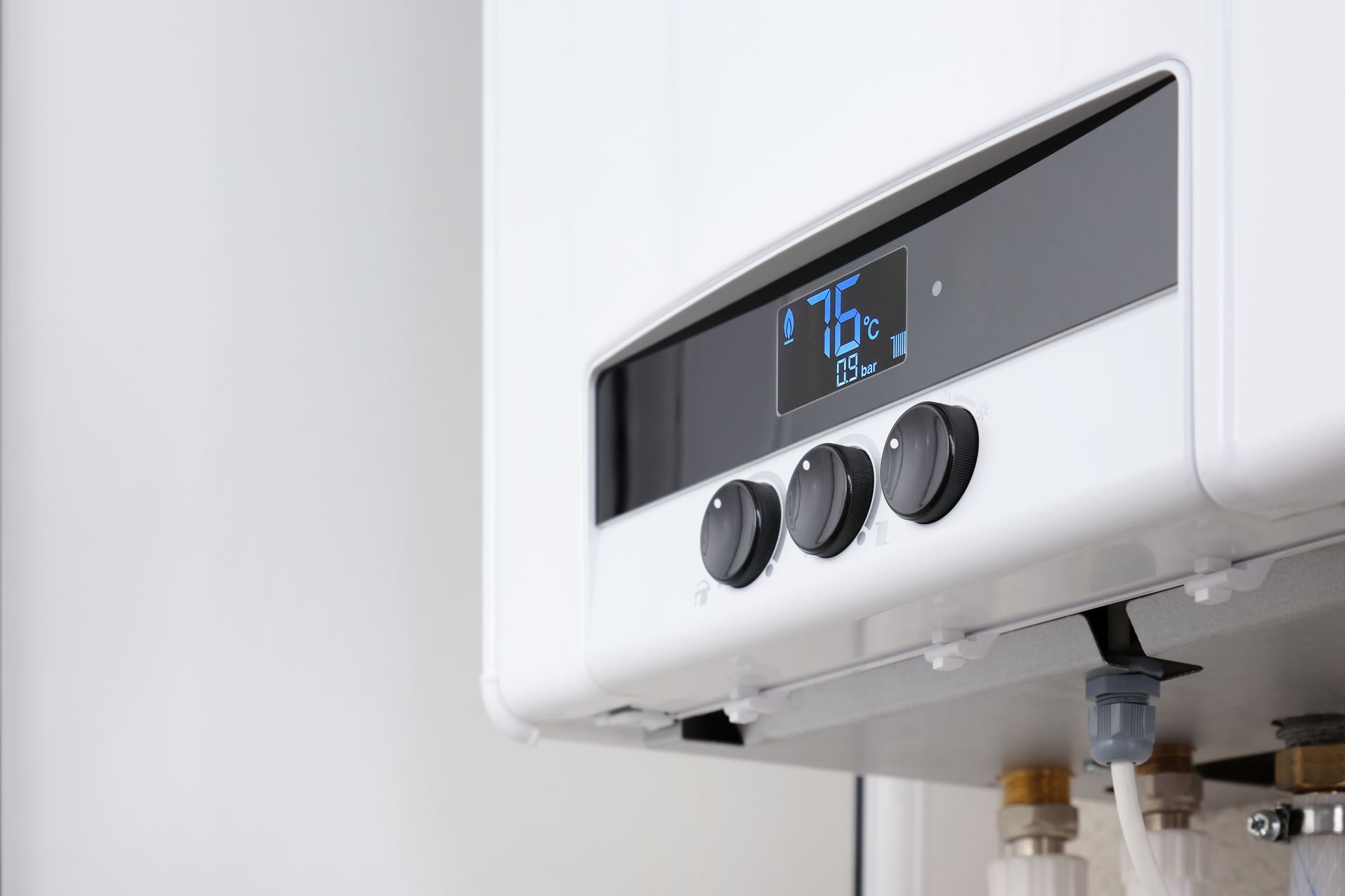 White wall-mounted boiler with a digital display showing 76 degrees and control knobs; copper pipes below.