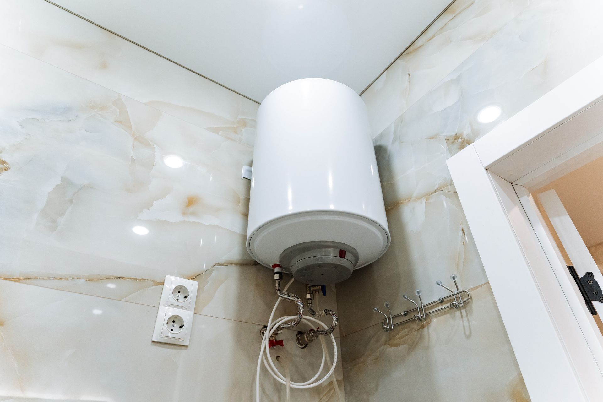 White water heater mounted on a marble wall, near a door and electrical outlets.