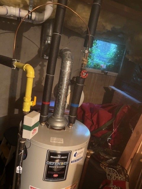 A plumber in blue overalls works under a sink, using a wrench on pipes.
