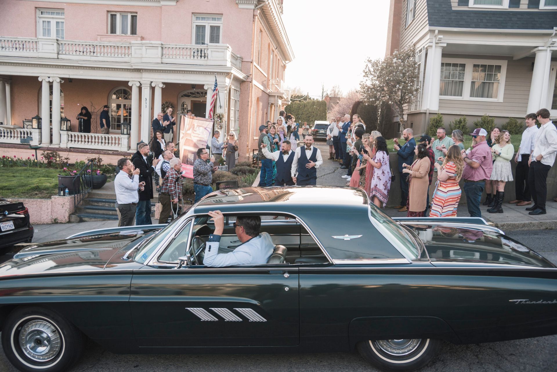 A man is driving a car down a street while a crowd watches.