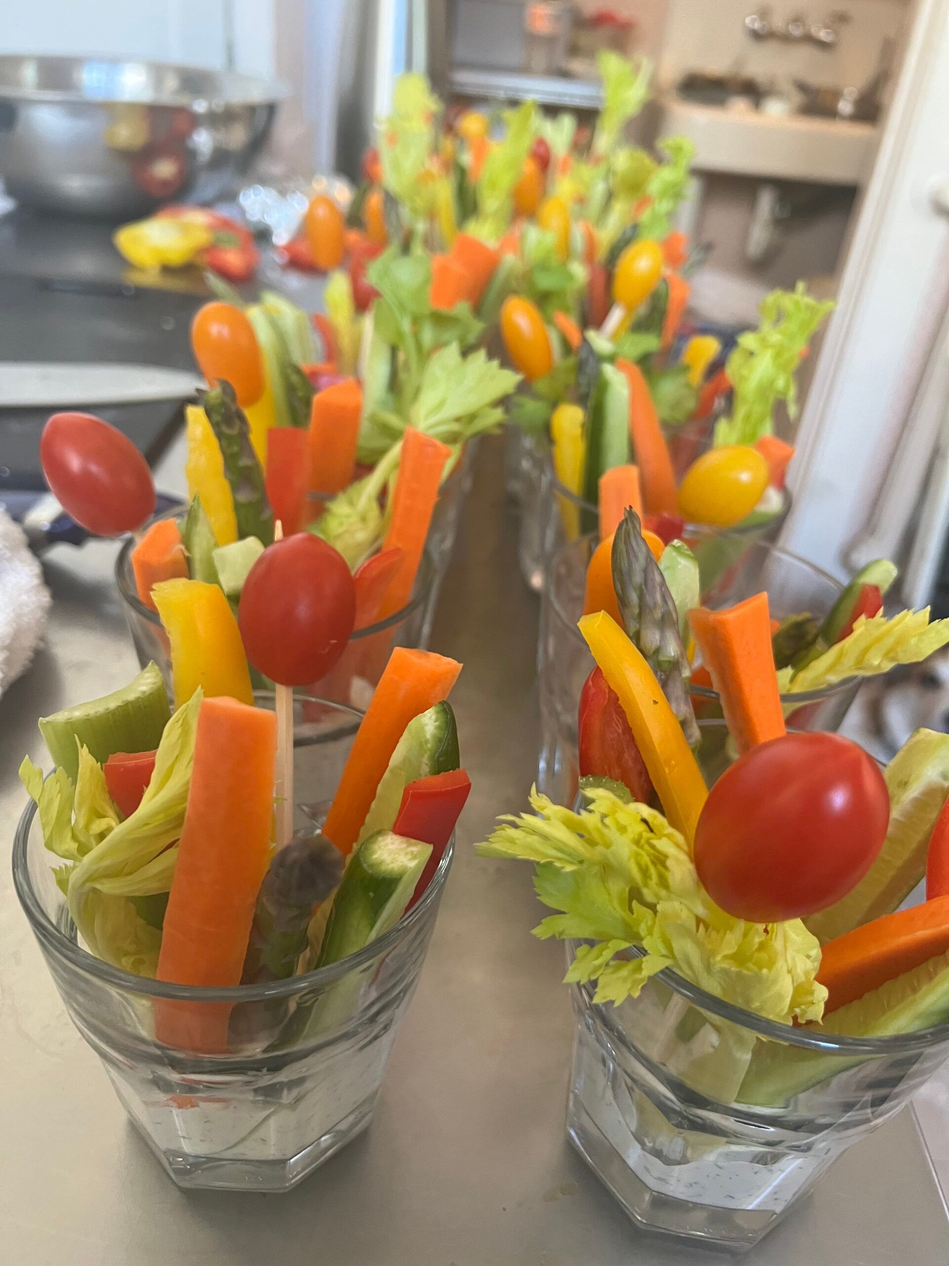 A bunch of glasses filled with vegetables and tomatoes on a table.