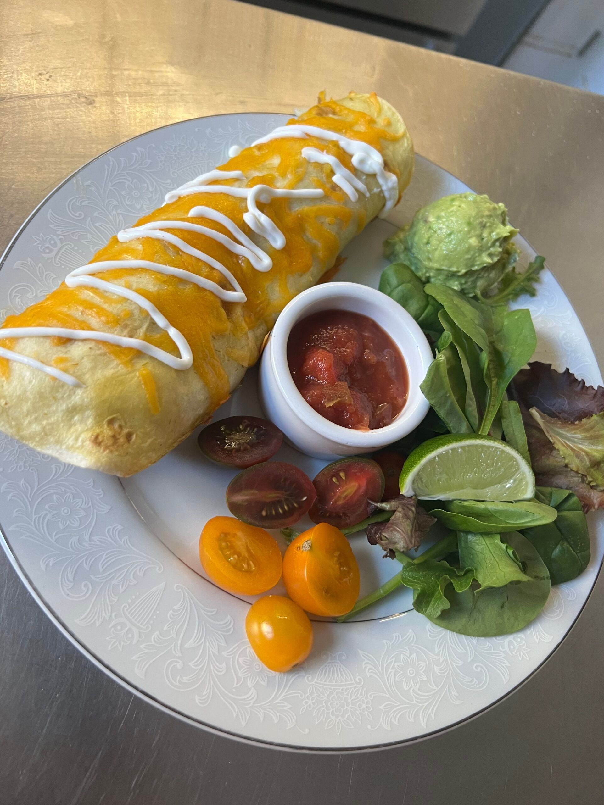 A burrito with salsa , guacamole and tomatoes on a plate.
