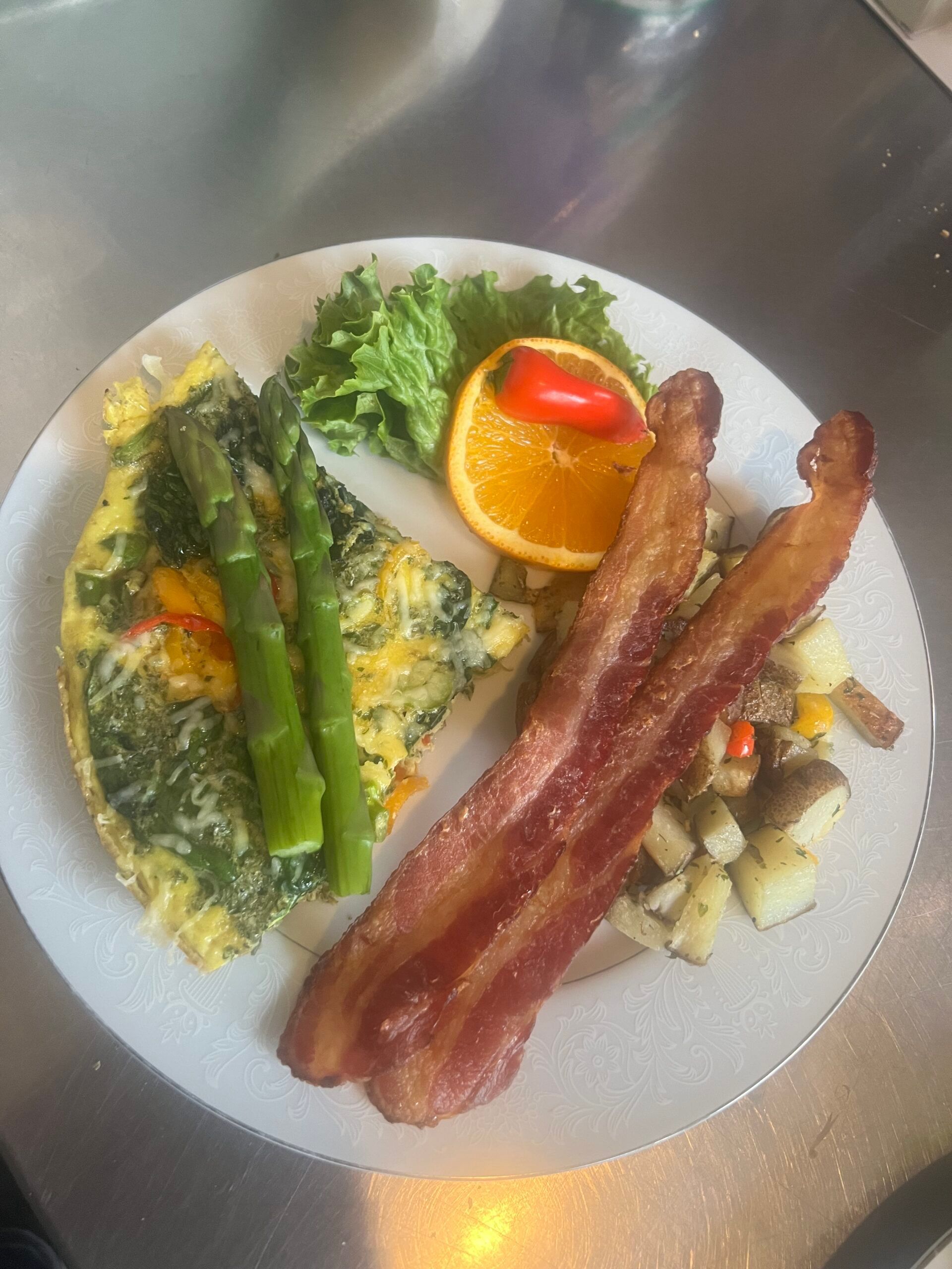 A plate of food with eggs , bacon , asparagus and potatoes on a table.