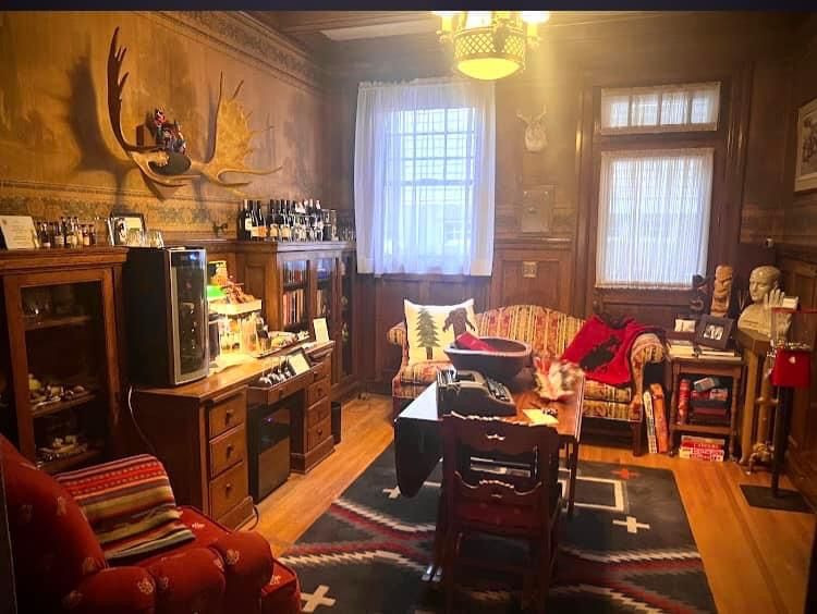A living room with a couch , chairs , table and a moose head on the wall.