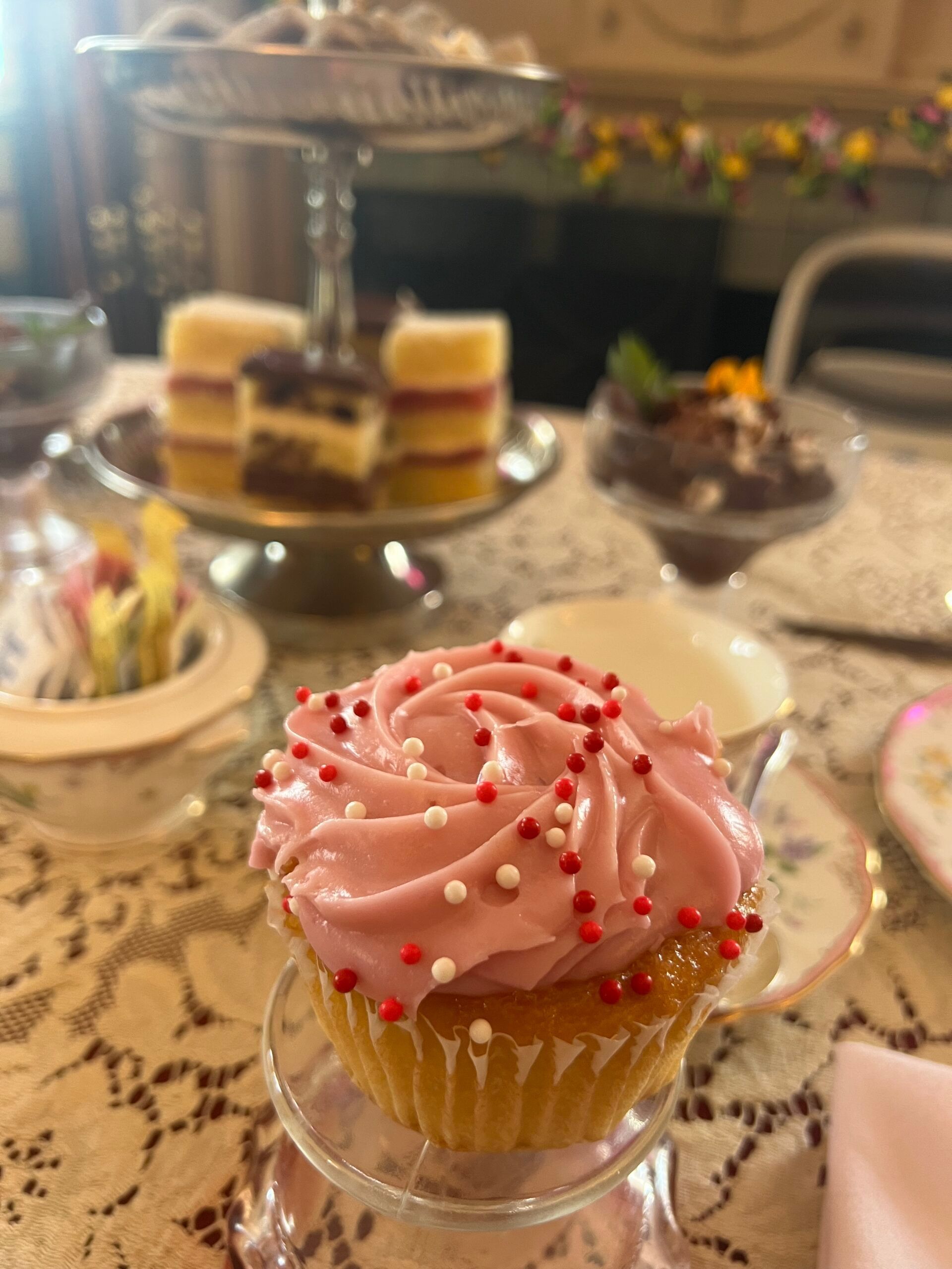 A close up of a cupcake with pink frosting and sprinkles on a table.