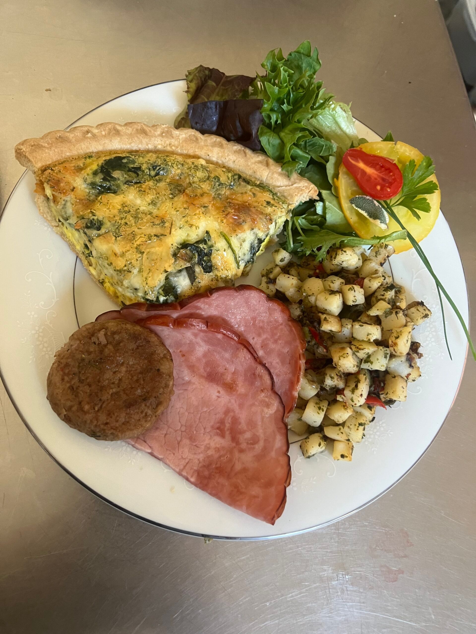 A white plate topped with a quiche , ham , potatoes , and vegetables.