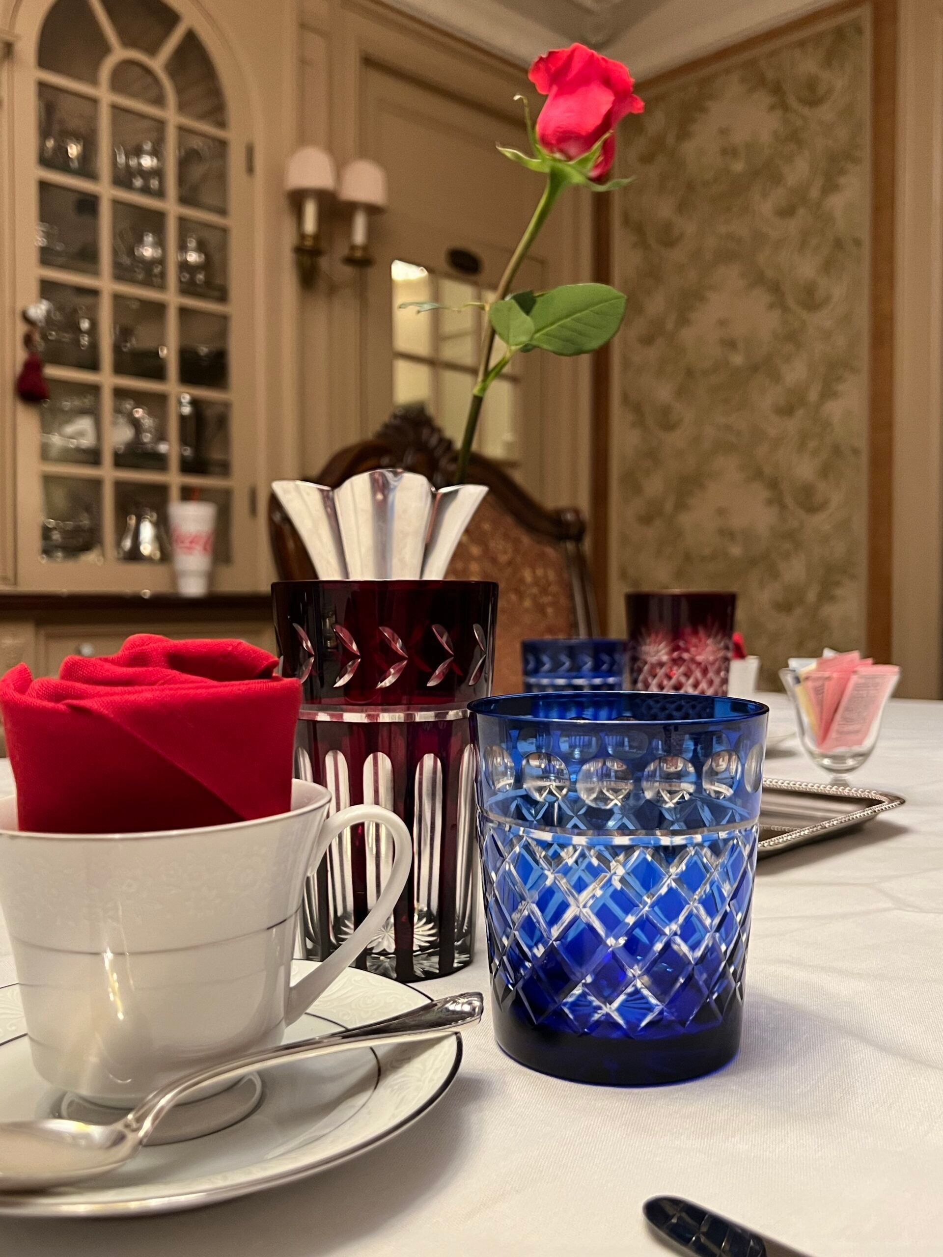 A table with a blue glass and a red rose in a vase