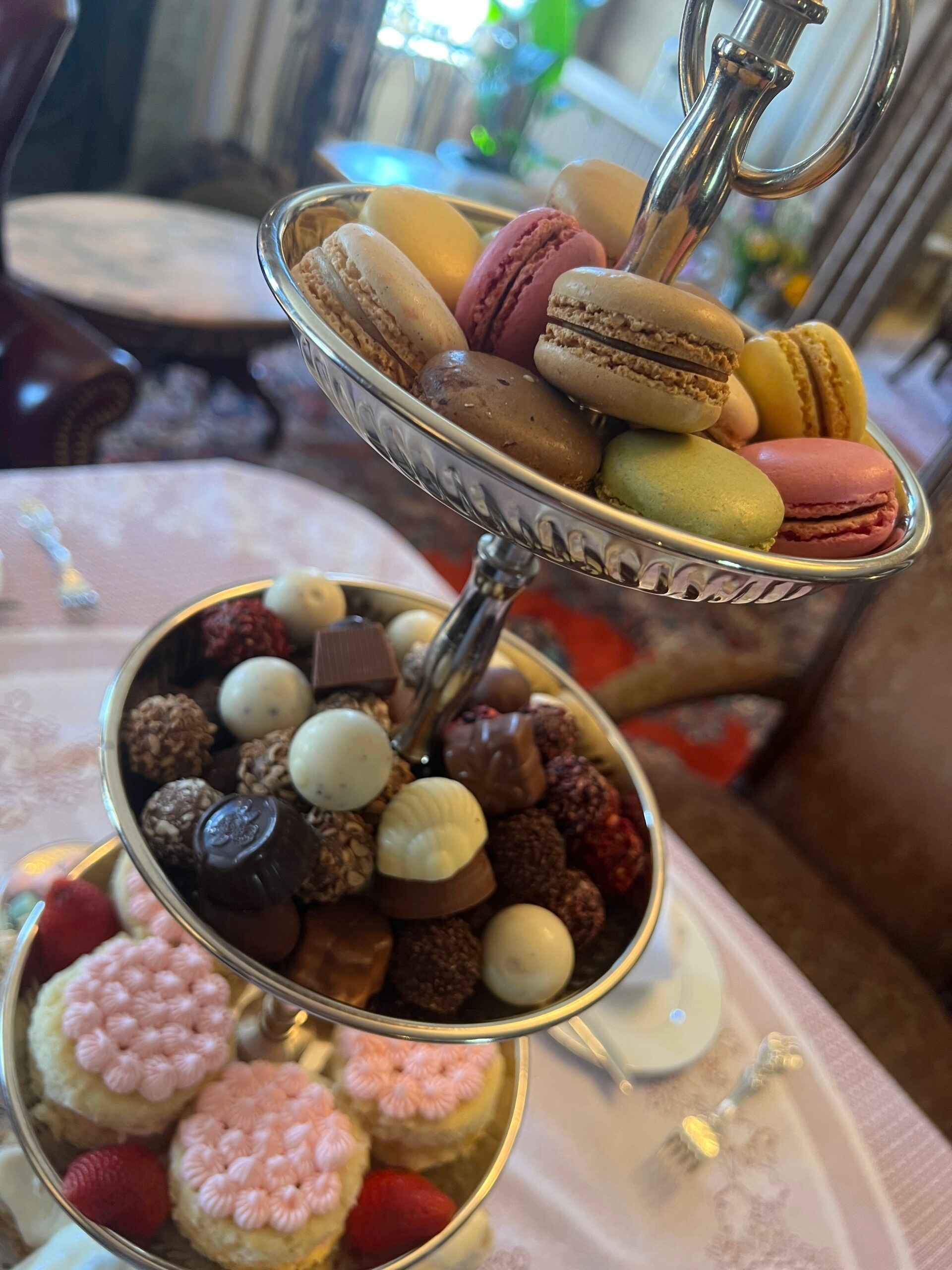 A three tiered tray filled with macarons , chocolates , and cookies on a table.