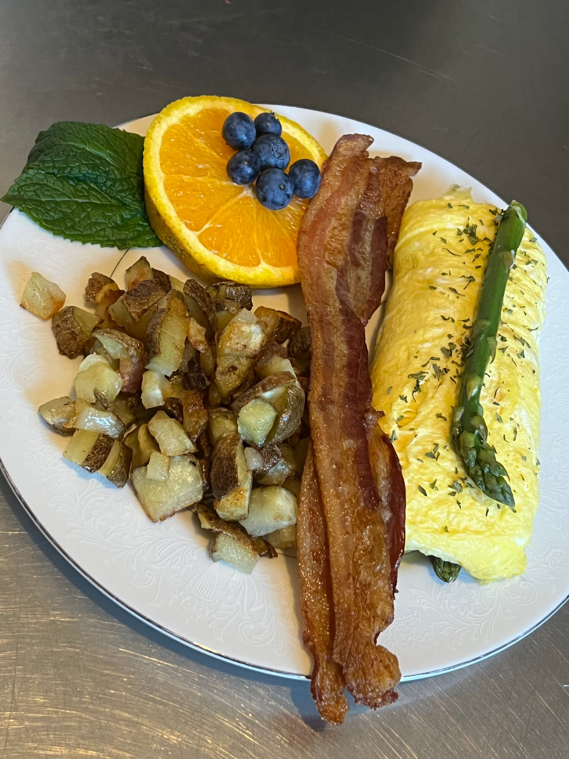 A plate of food with eggs , bacon , potatoes and blueberries on a table.