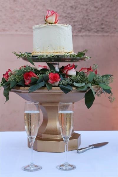 A wedding cake sitting on top of a cake stand next to two glasses of champagne