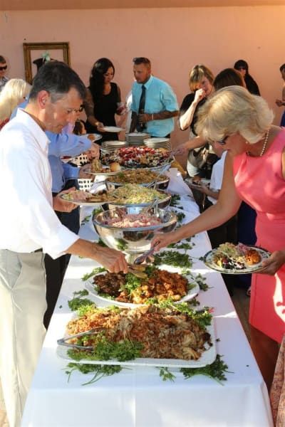 A group of people are standing around a table with plates of food on it