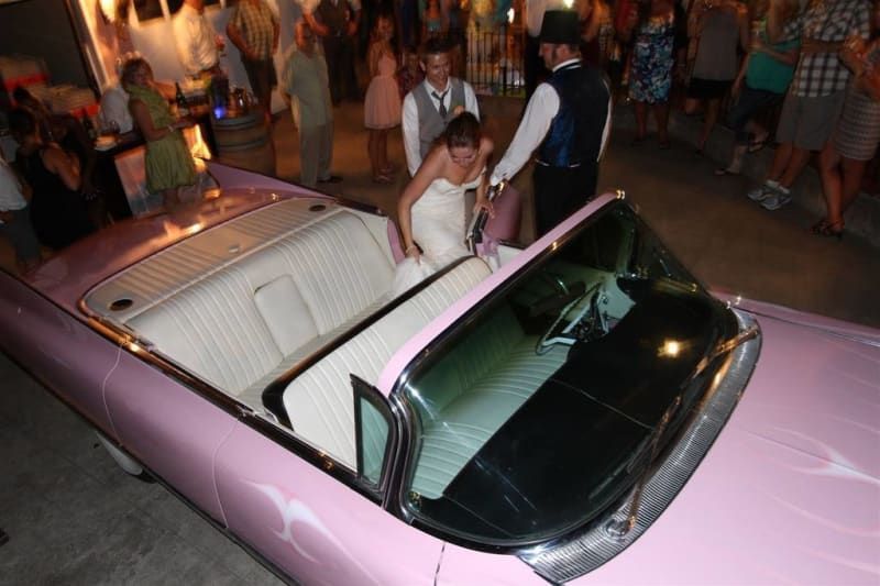 A bride and groom are getting out of a pink convertible car.