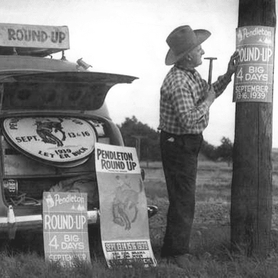 A black and white photo of a man standing next to a sign that says round up