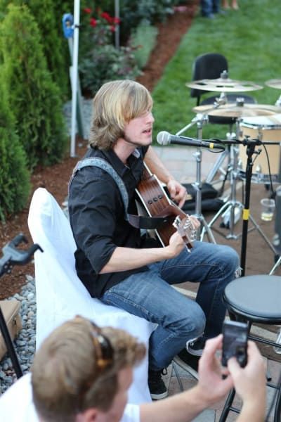 A man is playing a guitar while another man takes a picture
