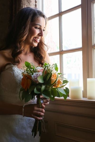 A woman in a wedding dress is holding a bouquet of flowers and looking out a window.