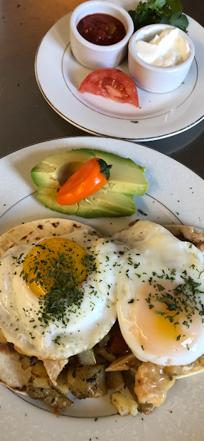 Two plates of food with eggs , avocado and tomatoes on a table.