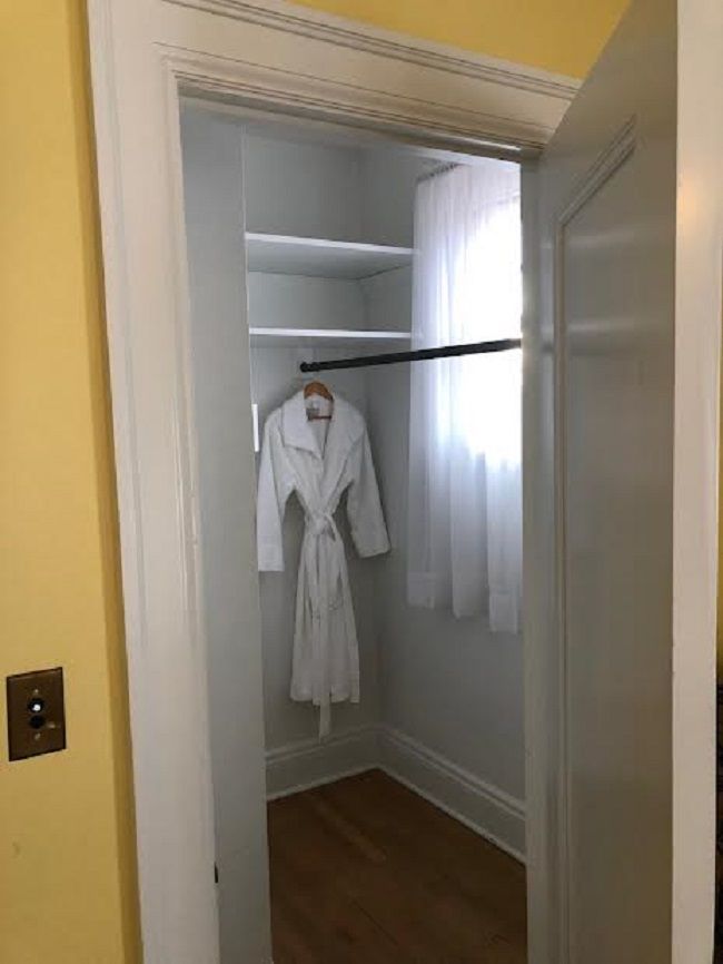 A white robe is hanging in a closet next to a window.