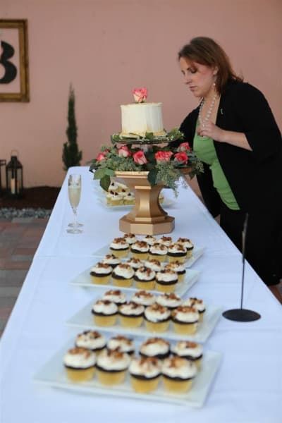 A woman stands at a table with cupcakes and a cake