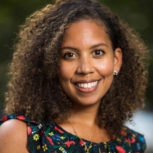 Junge Person mit geflochtenen Haaren lächelt, im Freien, weicher Hintergrund.