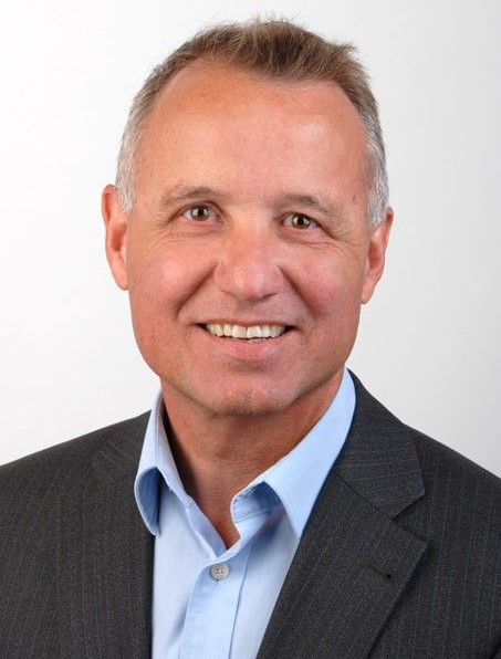 Junge Person mit geflochtenen Haaren lächelt, im Freien, weicher Hintergrund.