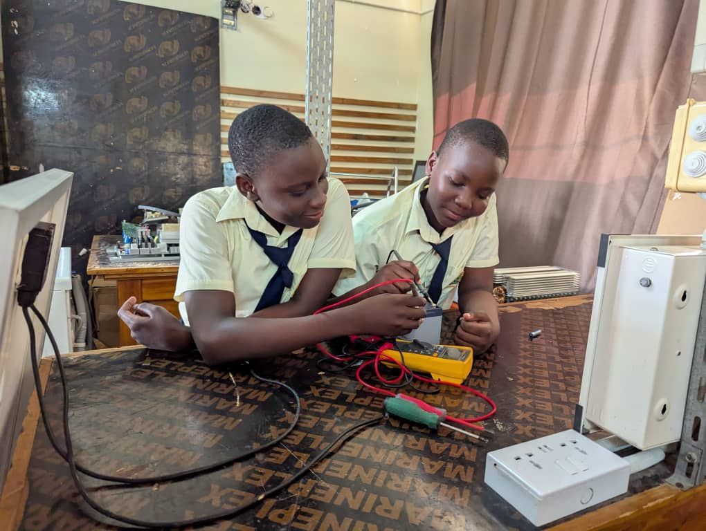 Kinder in orangefarbenen Uniformen winken und lächeln in einem hell erleuchteten Klassenzimmer.