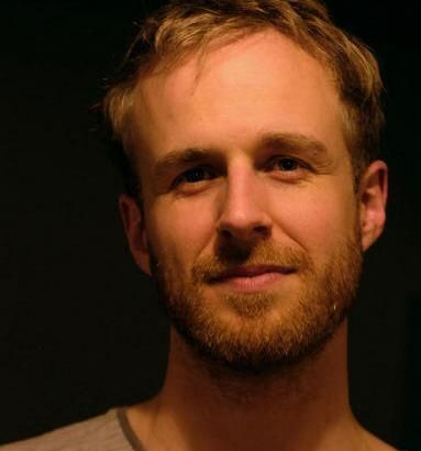 Junge Person mit geflochtenen Haaren lächelt, im Freien, weicher Hintergrund.