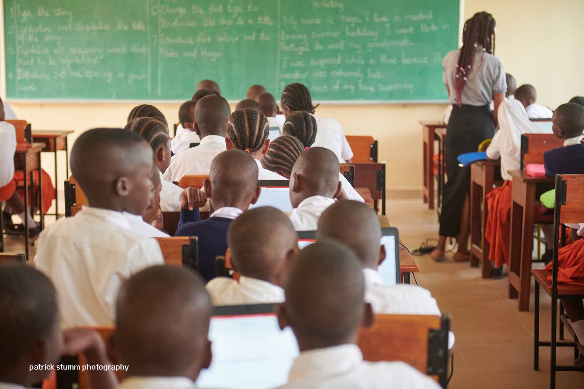 Eine Gruppe von Schülerinnen in roten Kleidern und schwarzen Hemden posiert mit ihren Lehrern vor einem Gebäude.
