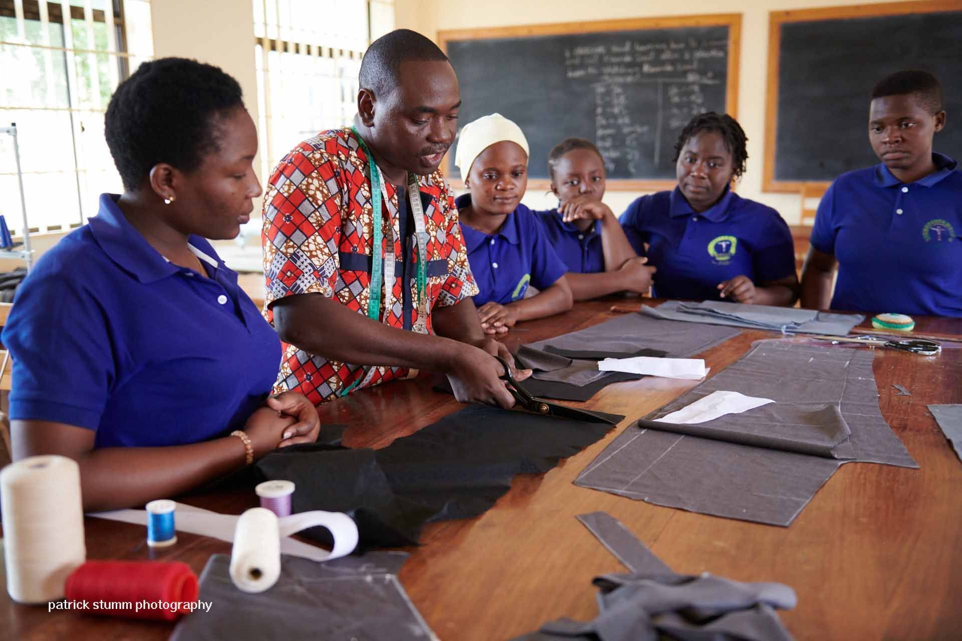 Kinder in orangefarbenen Schuluniformen posieren lächelnd und winkend in einem Klassenzimmer.