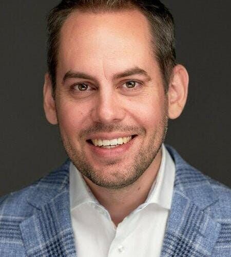 Junge Person mit geflochtenen Haaren lächelt, im Freien, weicher Hintergrund.