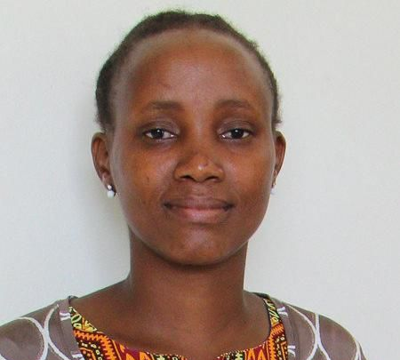 Junge Person mit geflochtenen Haaren lächelt, im Freien, weicher Hintergrund.