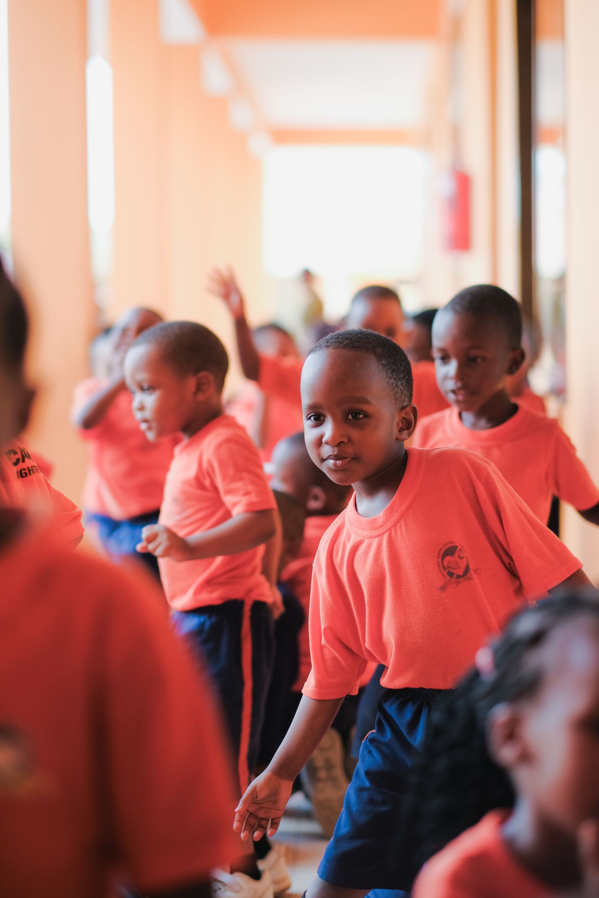 Kinder in orange-weißen Schuluniformen, einige winken.