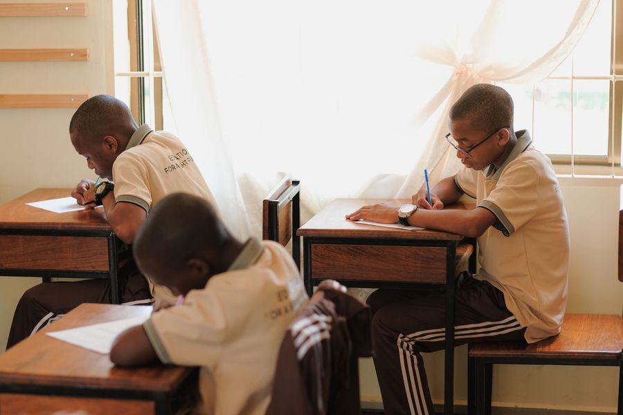 Ein Mädchen faltet Stoff auf einem Tisch in einem Klassenzimmer; im Hintergrund ist eine Tafel zu sehen.