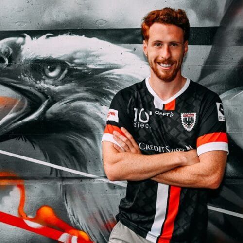 Junge Person mit geflochtenen Haaren lächelt, im Freien, weicher Hintergrund.