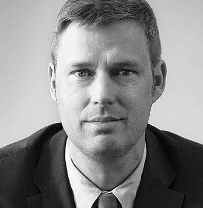 Junge Person mit geflochtenen Haaren lächelt, im Freien, weicher Hintergrund.