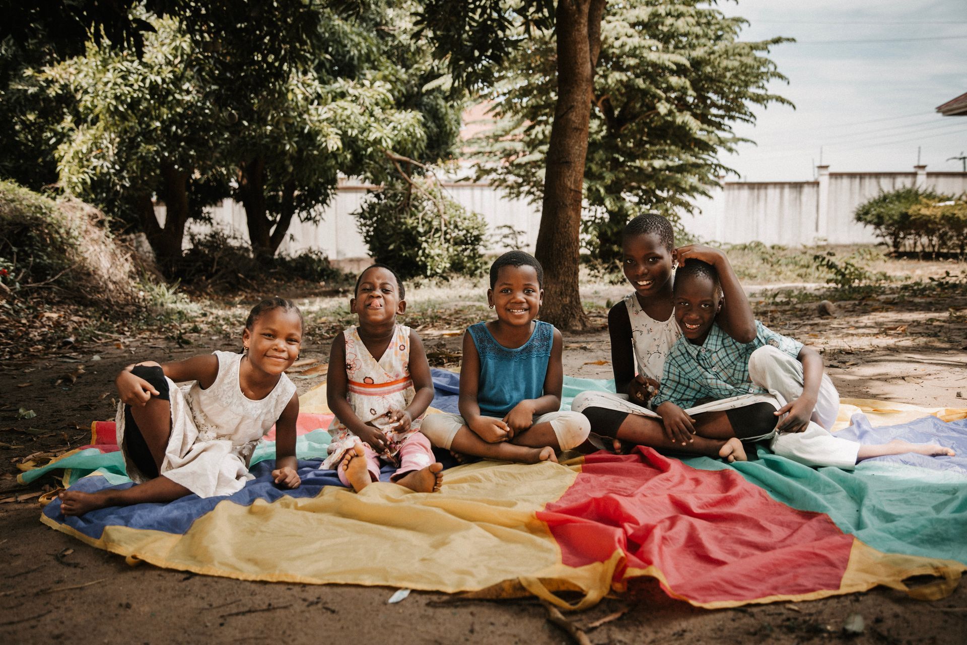 Kinder hocken auf dem Boden und malen mit Kreide. Eines hat einen bandagierten Arm. Draußen.