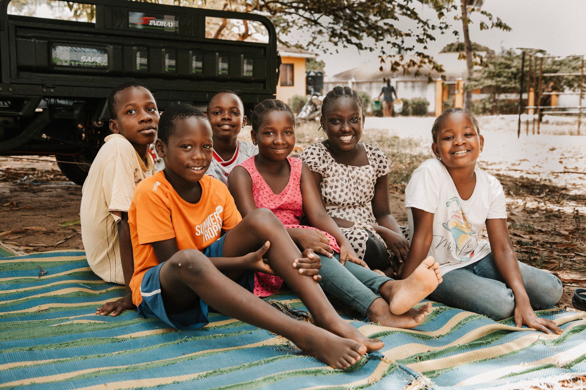 Eine Gruppe Kinder in orangefarbenen Schuluniformen lächelt und winkt drinnen.