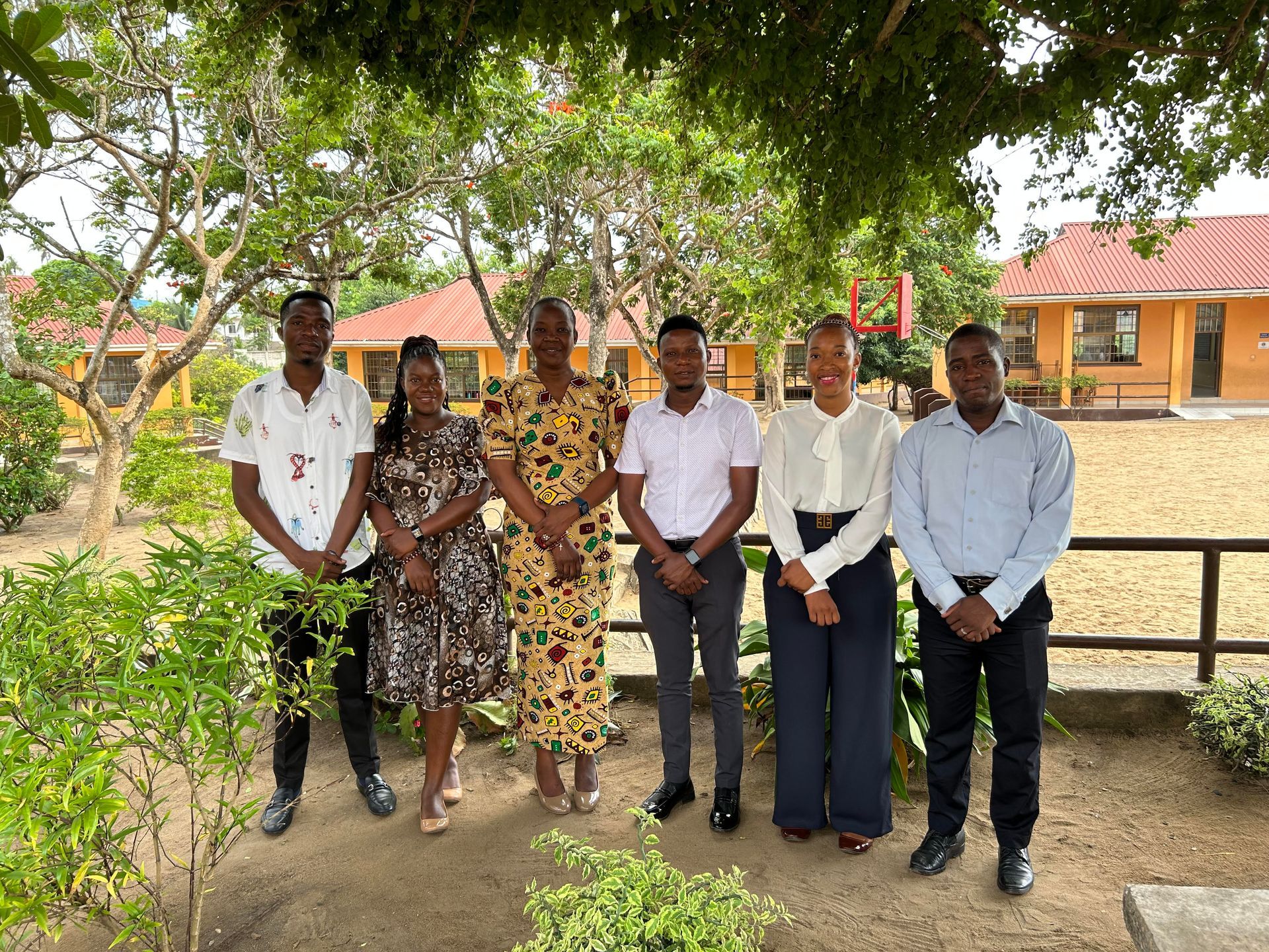 Vier Personen stehen an einem sonnigen Tag im Grünen. Zwei Männer und zwei Frauen posieren. Im Hintergrund ist ein Gebäude zu sehen.