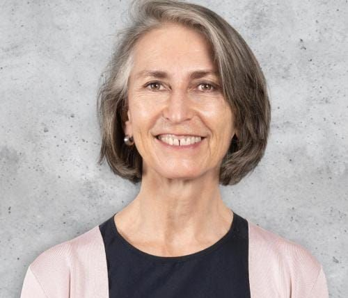 Junge Person mit geflochtenen Haaren lächelt, im Freien, weicher Hintergrund.