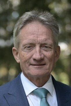 Junge Person mit geflochtenen Haaren lächelt, im Freien, weicher Hintergrund.