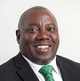 Junge Person mit geflochtenen Haaren lächelt, im Freien, weicher Hintergrund.