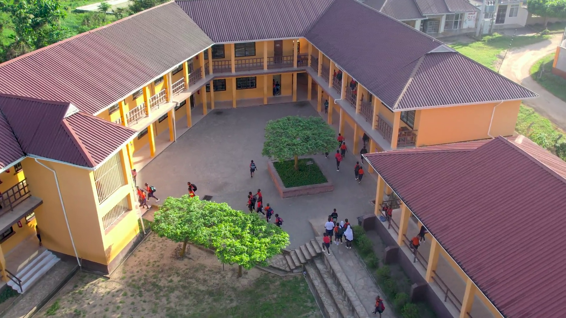 Luftaufnahme eines orangefarbenen, mehrstöckigen Schulgebäudes, das einen Innenhof mit Schülern umschließt.