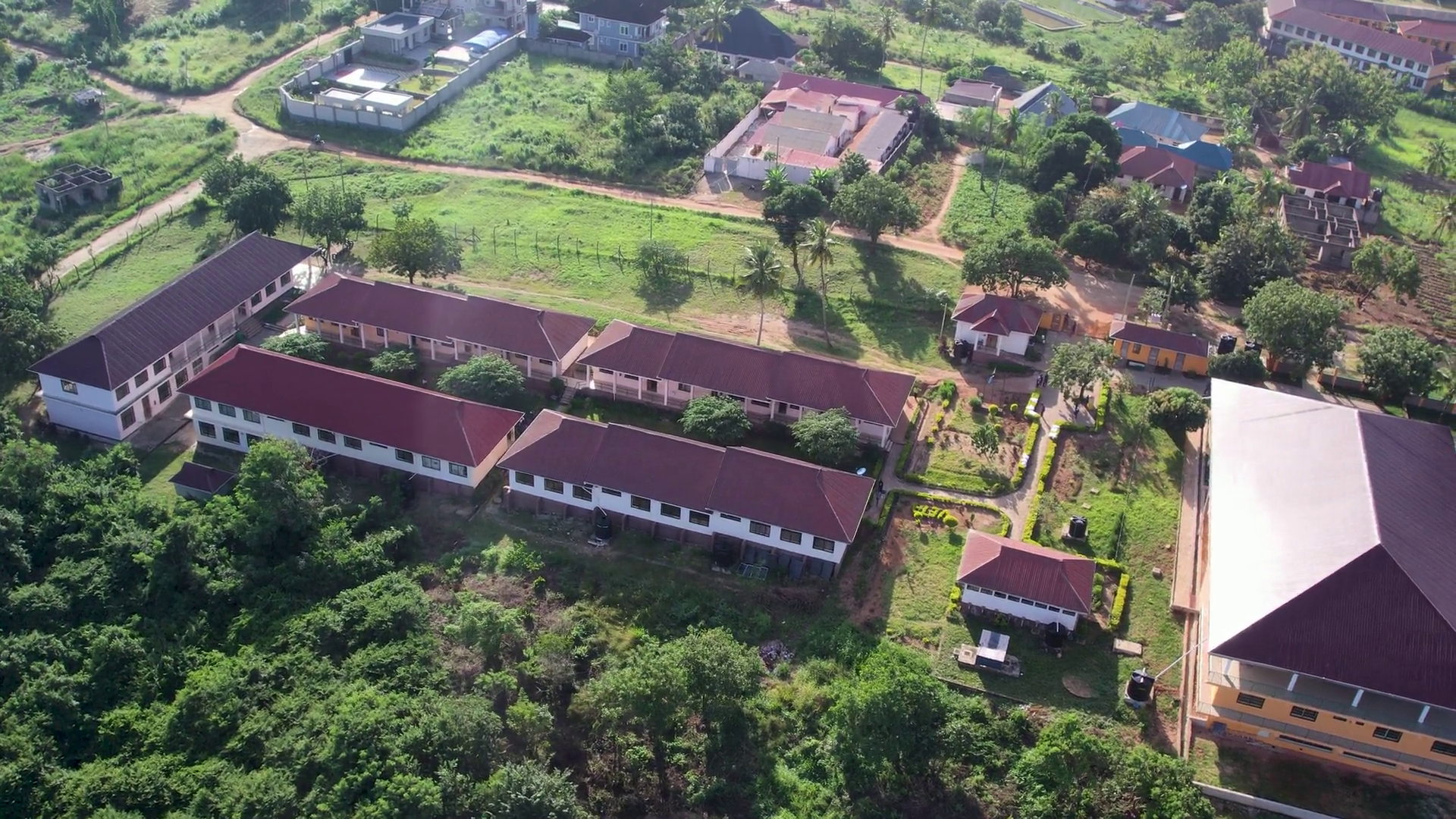 Luftaufnahme von Gebäuden mit roten Dächern, umgeben von grünen Bäumen und Gras.
