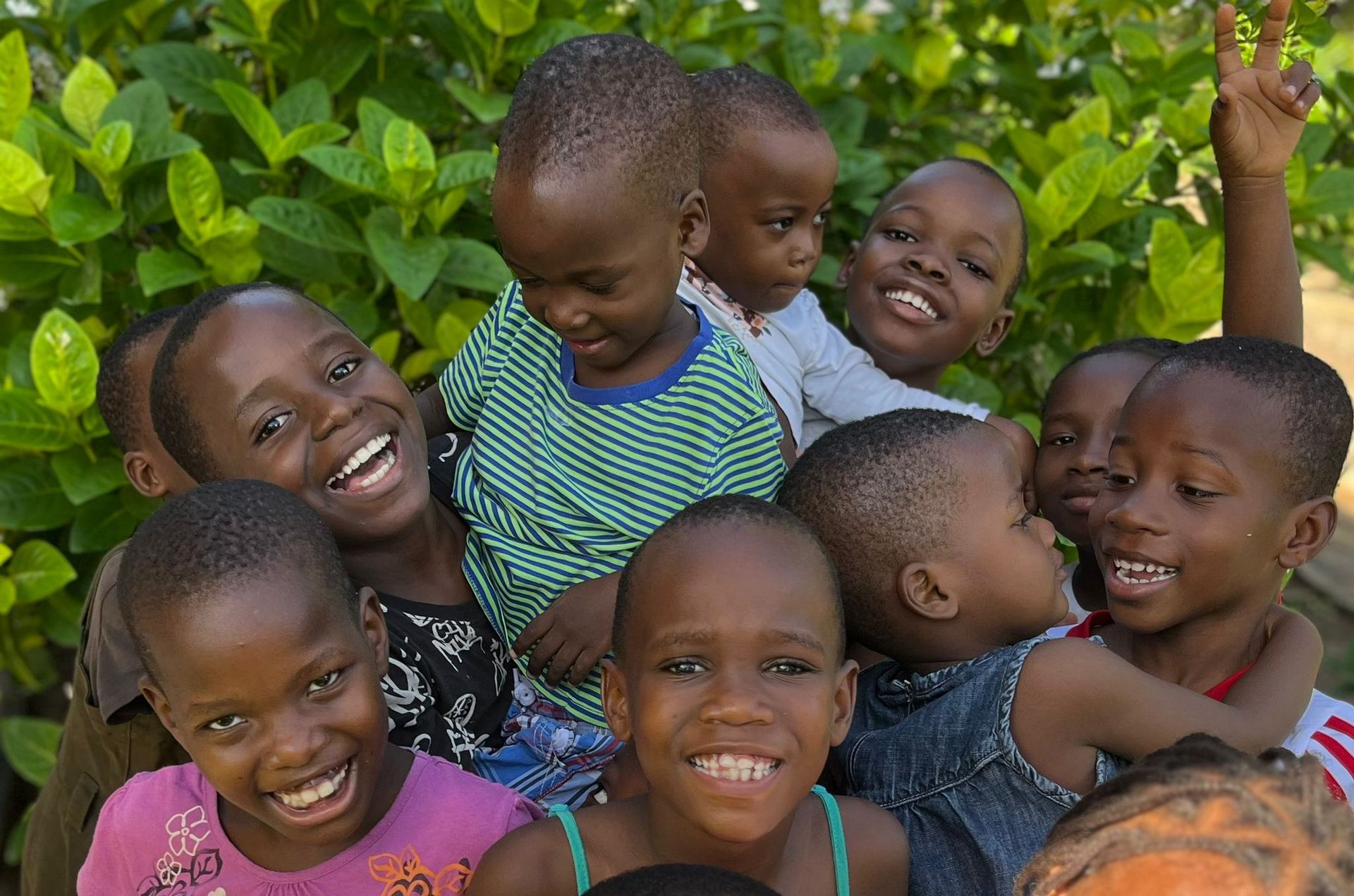 A group of happy children huddled together smiling in front of bright green foliage.