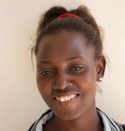 Frau mit dunkler Haut lächelt, die Frisur ist ein Dutt, vor grünem Hintergrund.