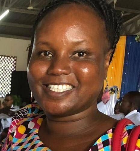 Frau mit dunkler Haut lächelt, die Frisur ist ein Dutt, vor grünem Hintergrund.