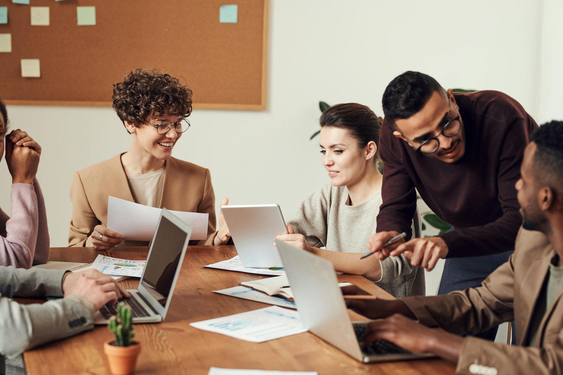 Group of people in an office meeting around a table with laptops and papers; discussing work.
