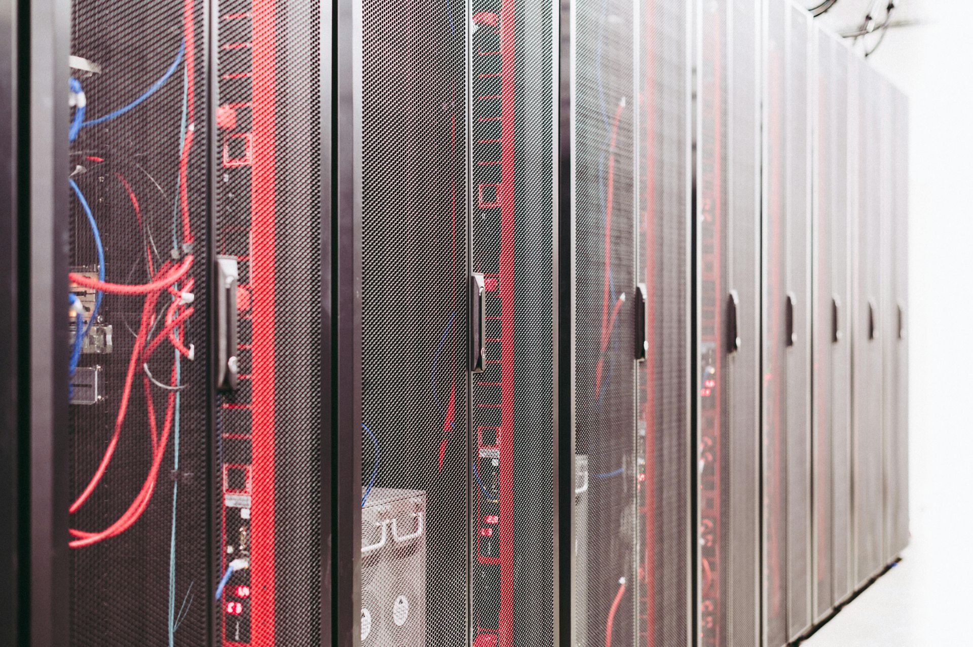 Rows of server racks in a data center, with red and blue cables visible inside open racks.