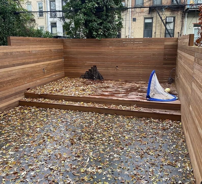A wooden fence surrounds a backyard filled with leaves.