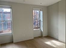 An empty room with two windows and a wooden floor.