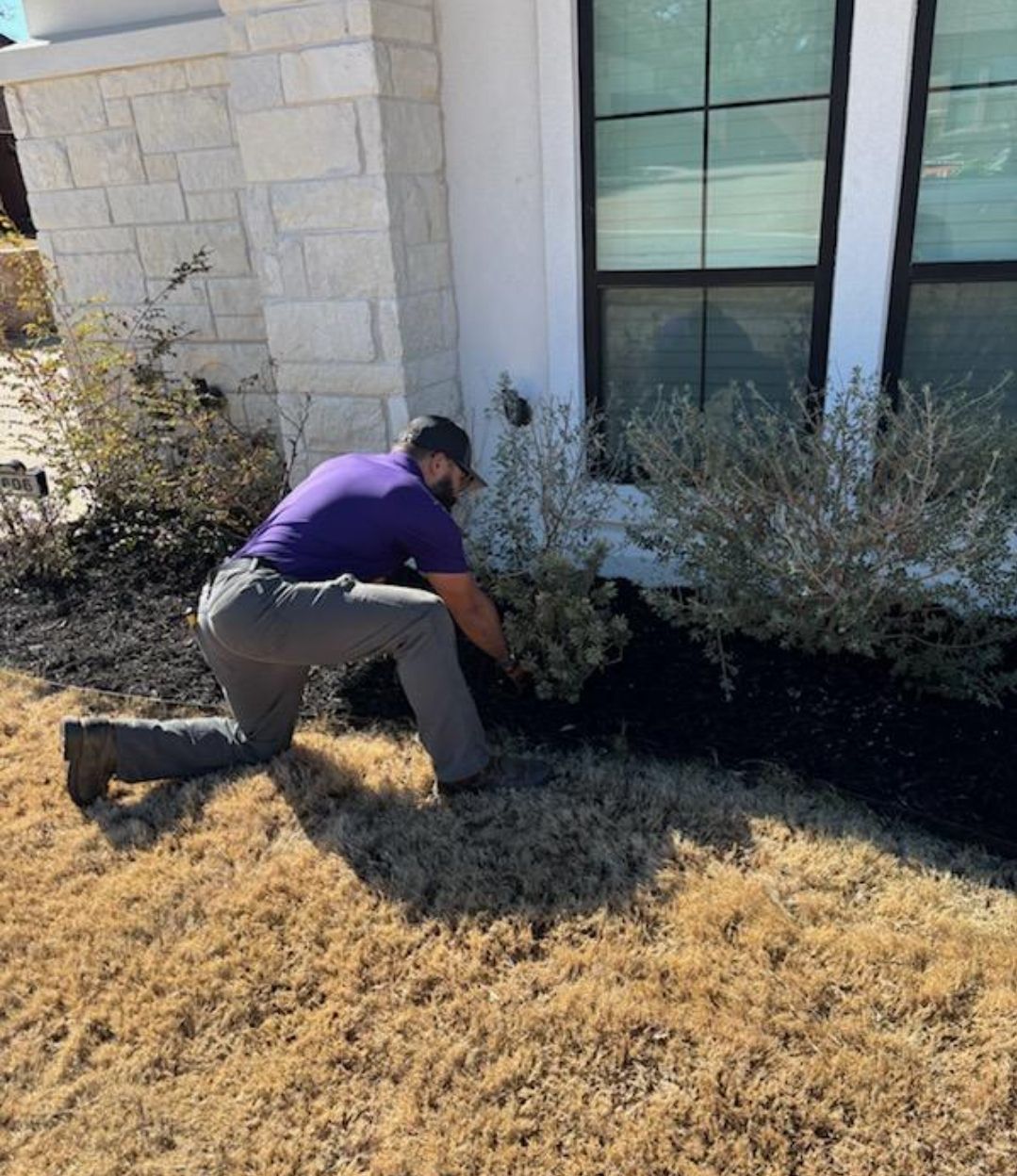 A man in a purple shirt is kneeling down in front of a house.